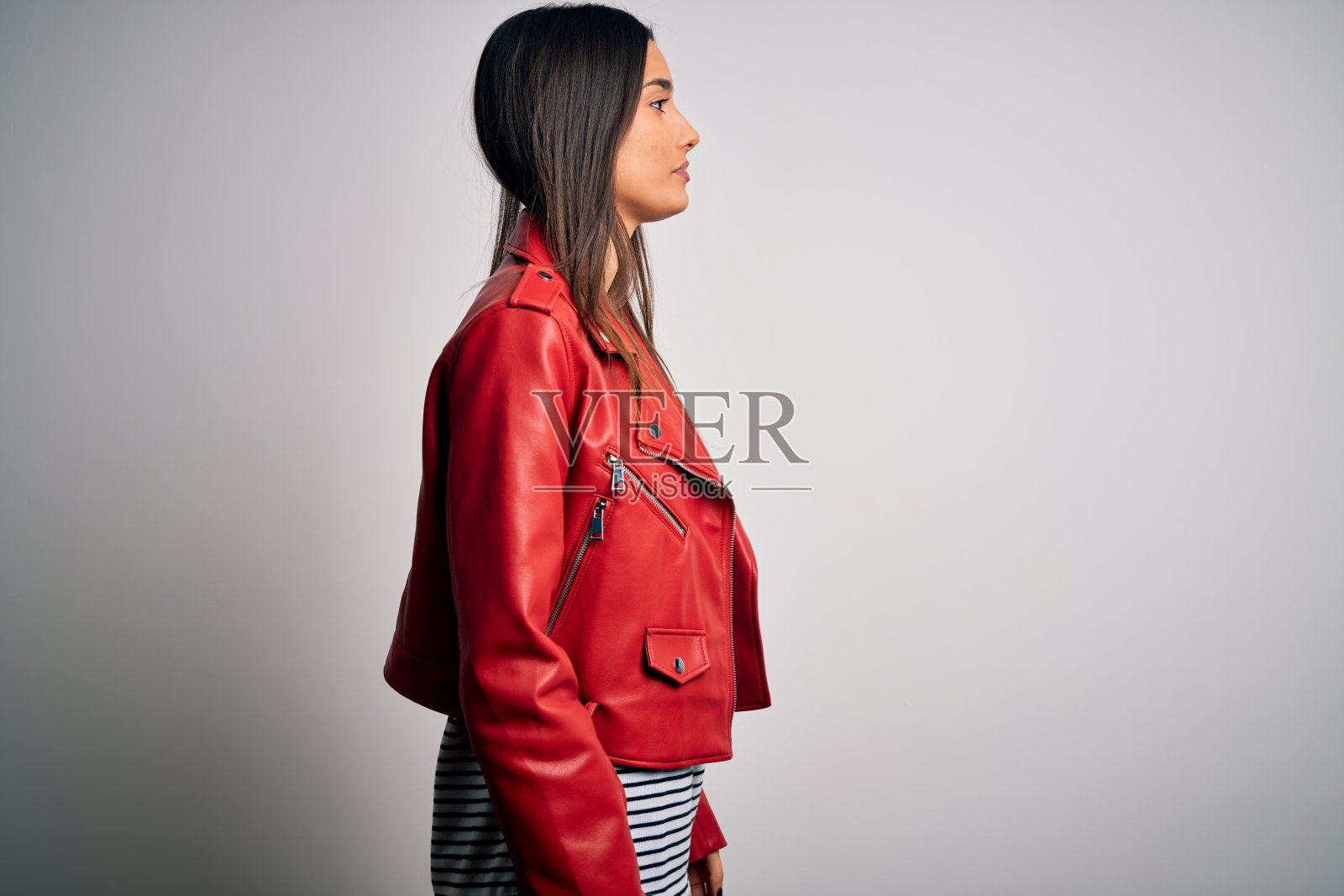 年轻美丽的黑发女子穿着休闲条纹t恤和红色夹克看向一边，放松的侧面姿势与自然的脸与自信的微笑。照片摄影图片