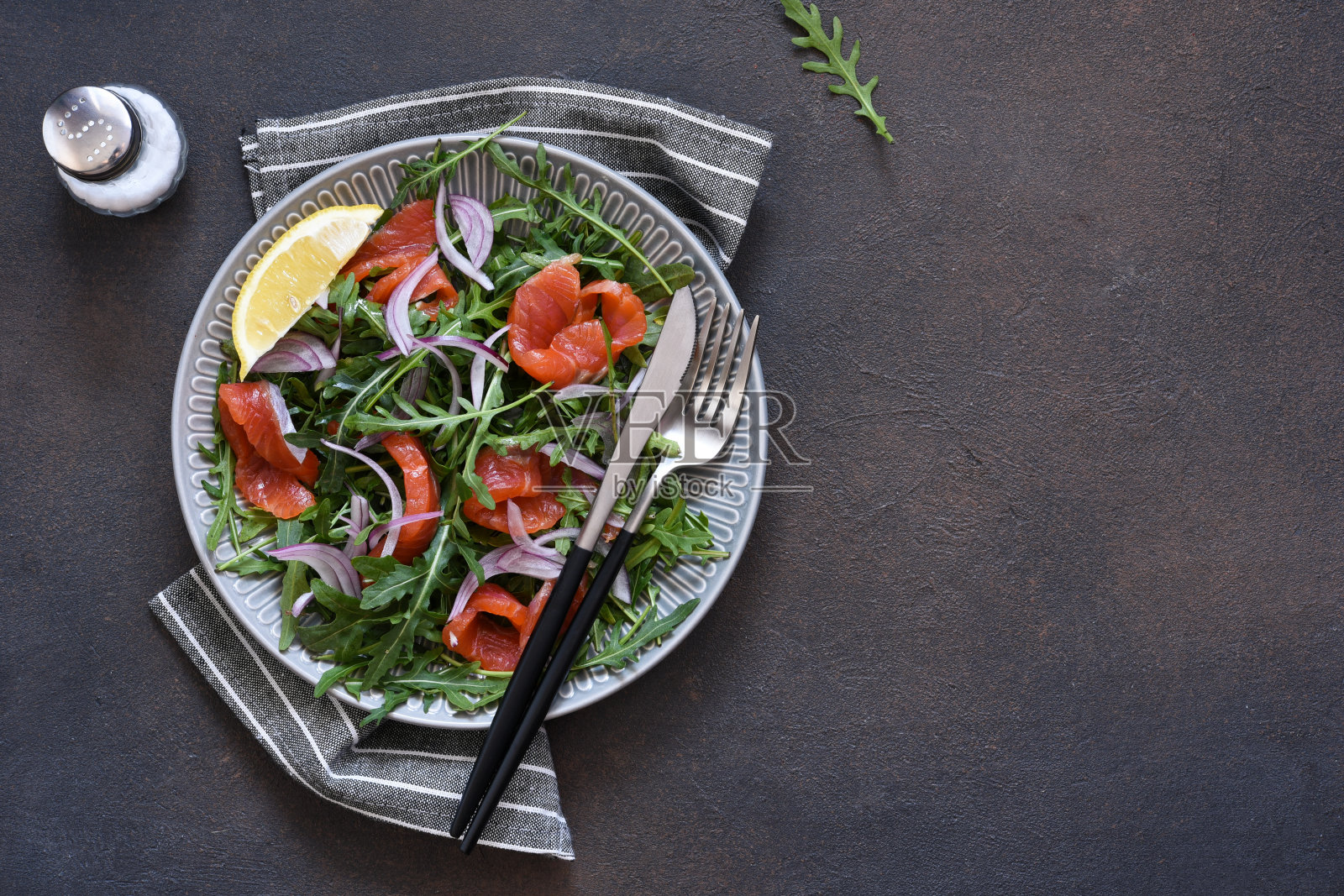 厨房昏暗的桌子上放着芝麻菜和鲑鱼沙拉。带有文本位置的俯视图。照片摄影图片