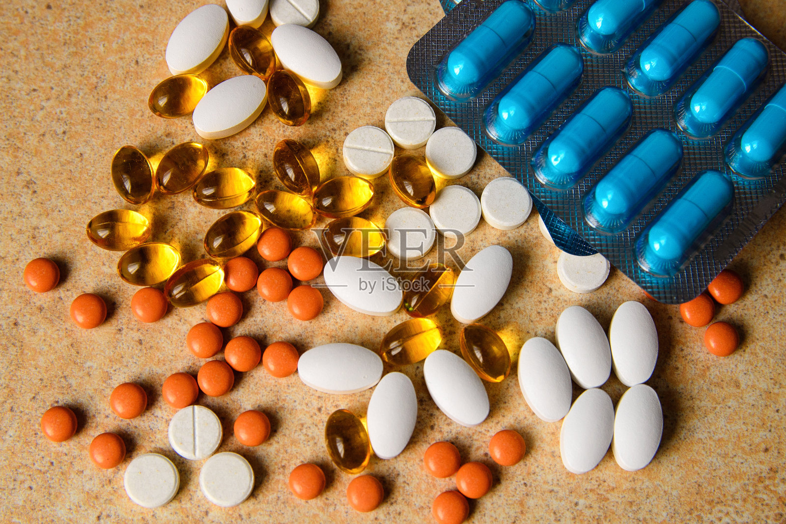 有蓝色、粉色和橙色药片、维生素D和鱼油胶囊的水疱随机地躺在沙质台面上照片摄影图片