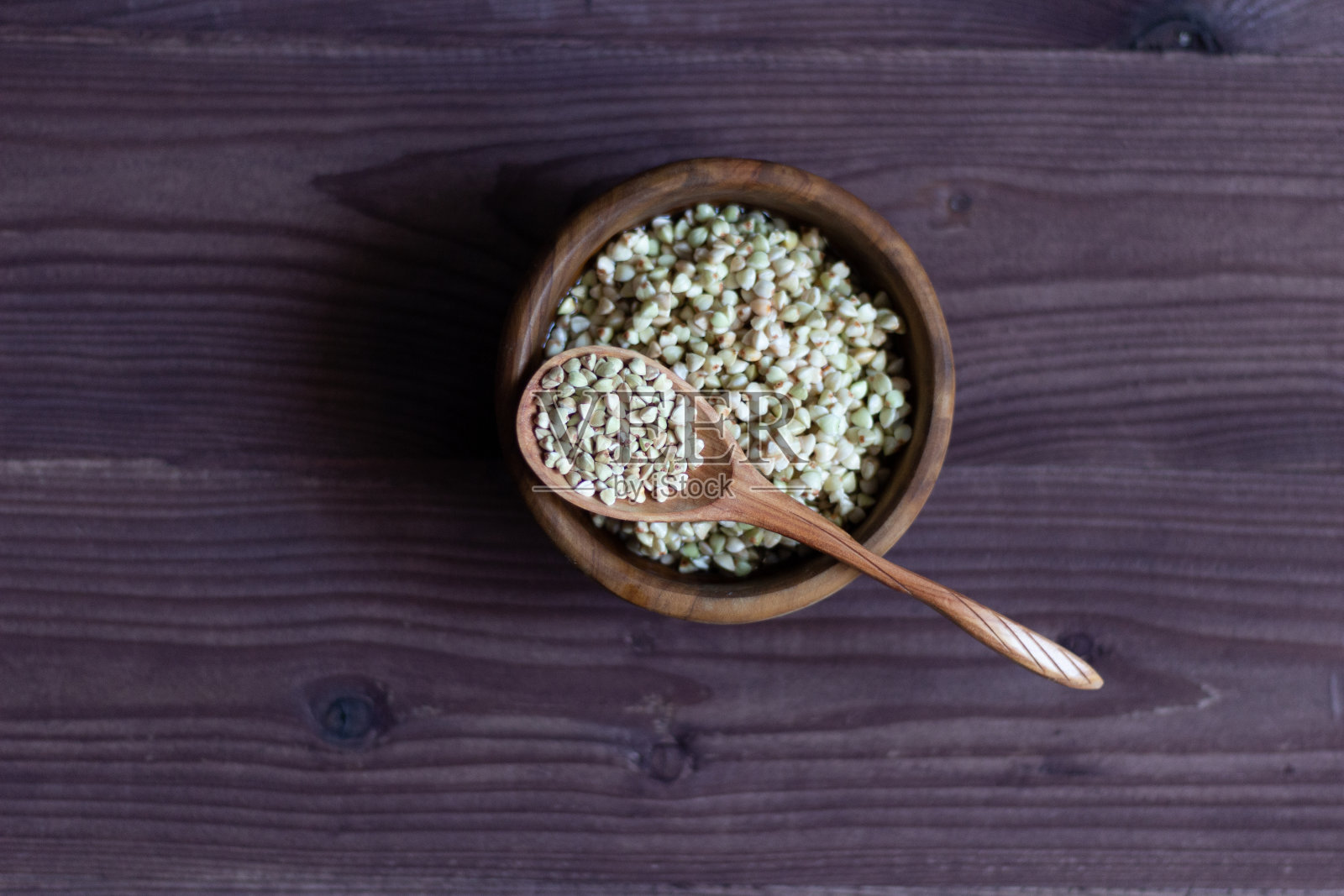 绿色荞麦堆在勺子和木碗在棕色的背景照片摄影图片