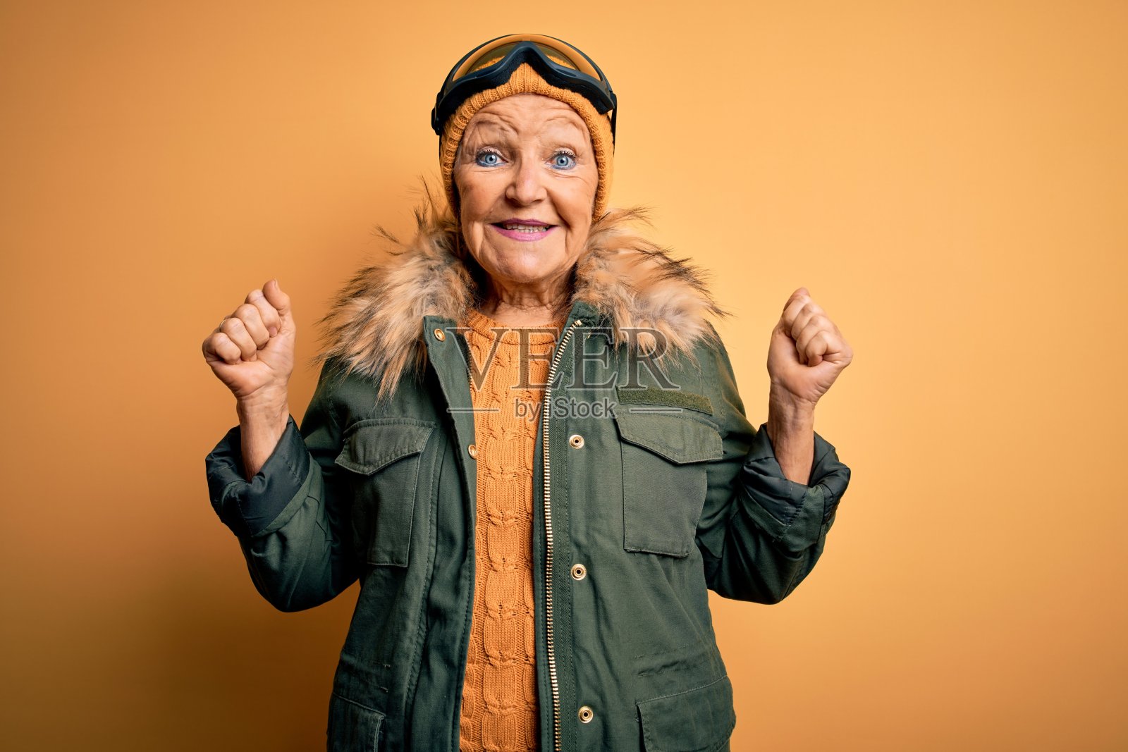 高级美丽的灰色头发的滑雪者女人穿着雪运动服和滑雪镜庆祝惊讶和惊讶的成功与手臂举起和睁开眼睛。赢家的概念。照片摄影图片