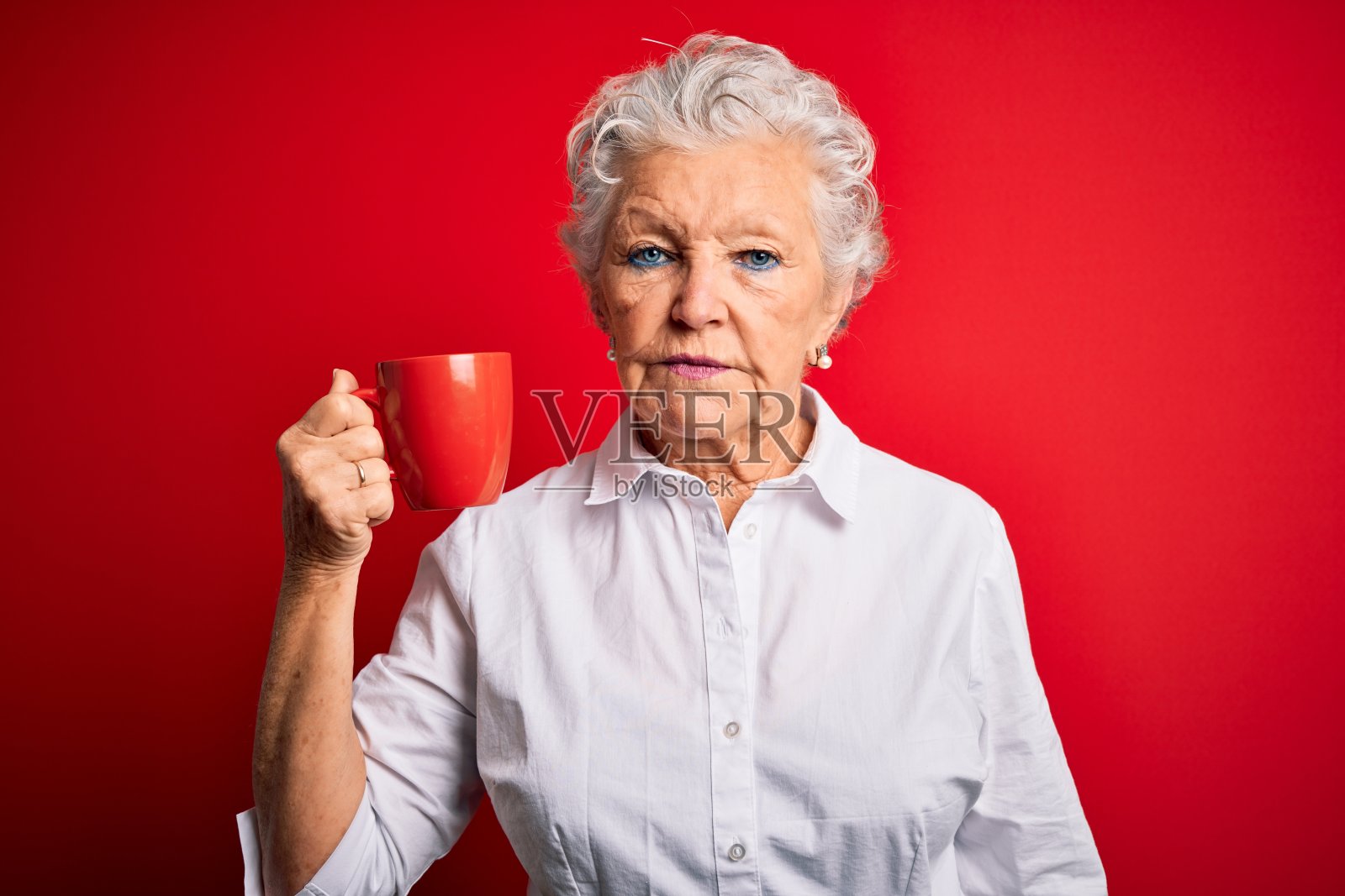 资深美女喝咖啡杯站在孤立的红色背景与自信的表情在聪明的脸思考严肃照片摄影图片