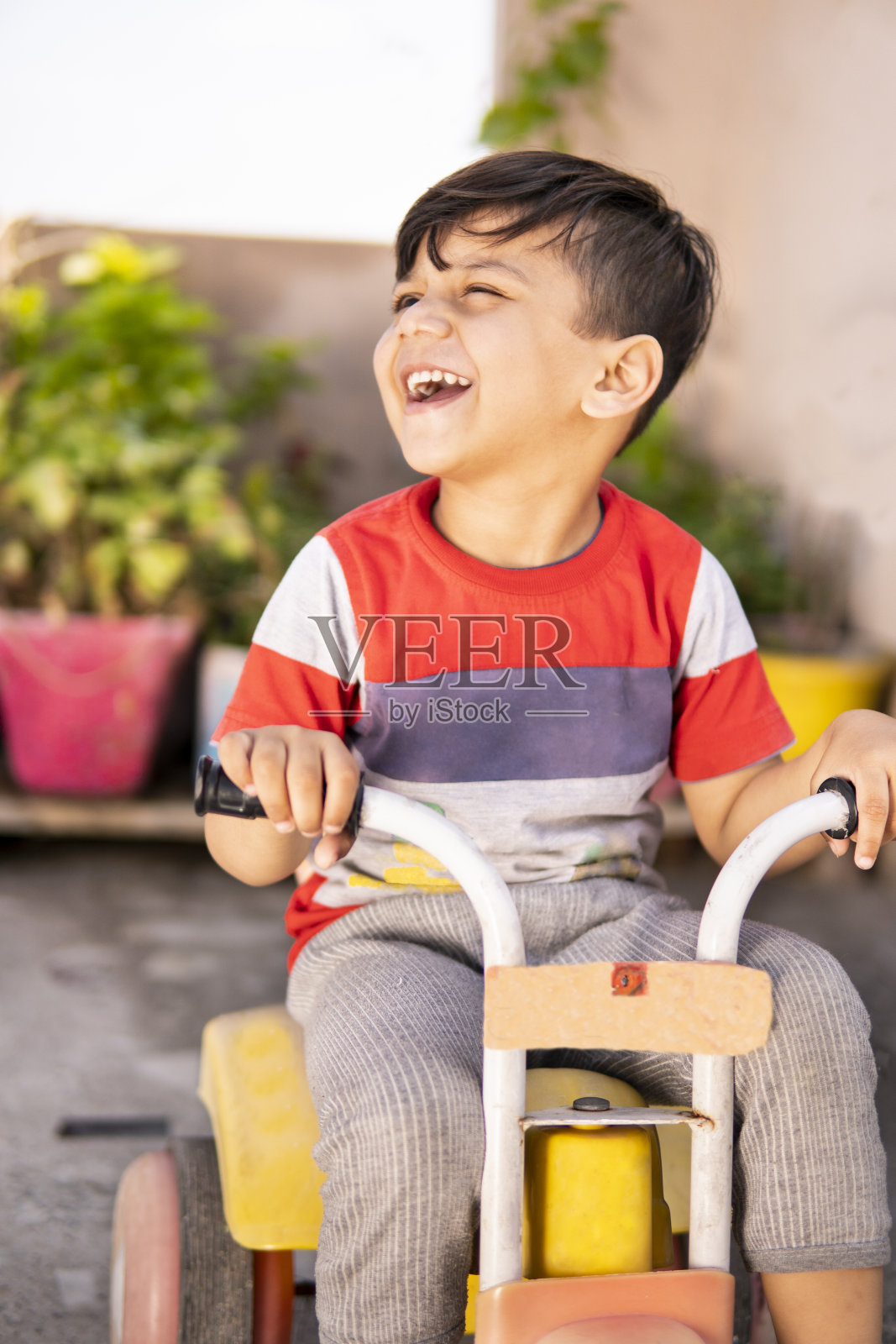 可爱的小男孩骑着三轮车在屋顶上。照片摄影图片