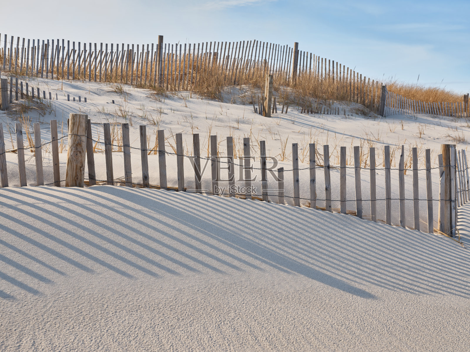 在新泽西岛海滩州立公园，用来保护沙丘免受风浪和人类侵蚀的防风栅栏，在傍晚的长影子突出了薄薄的木条照片摄影图片