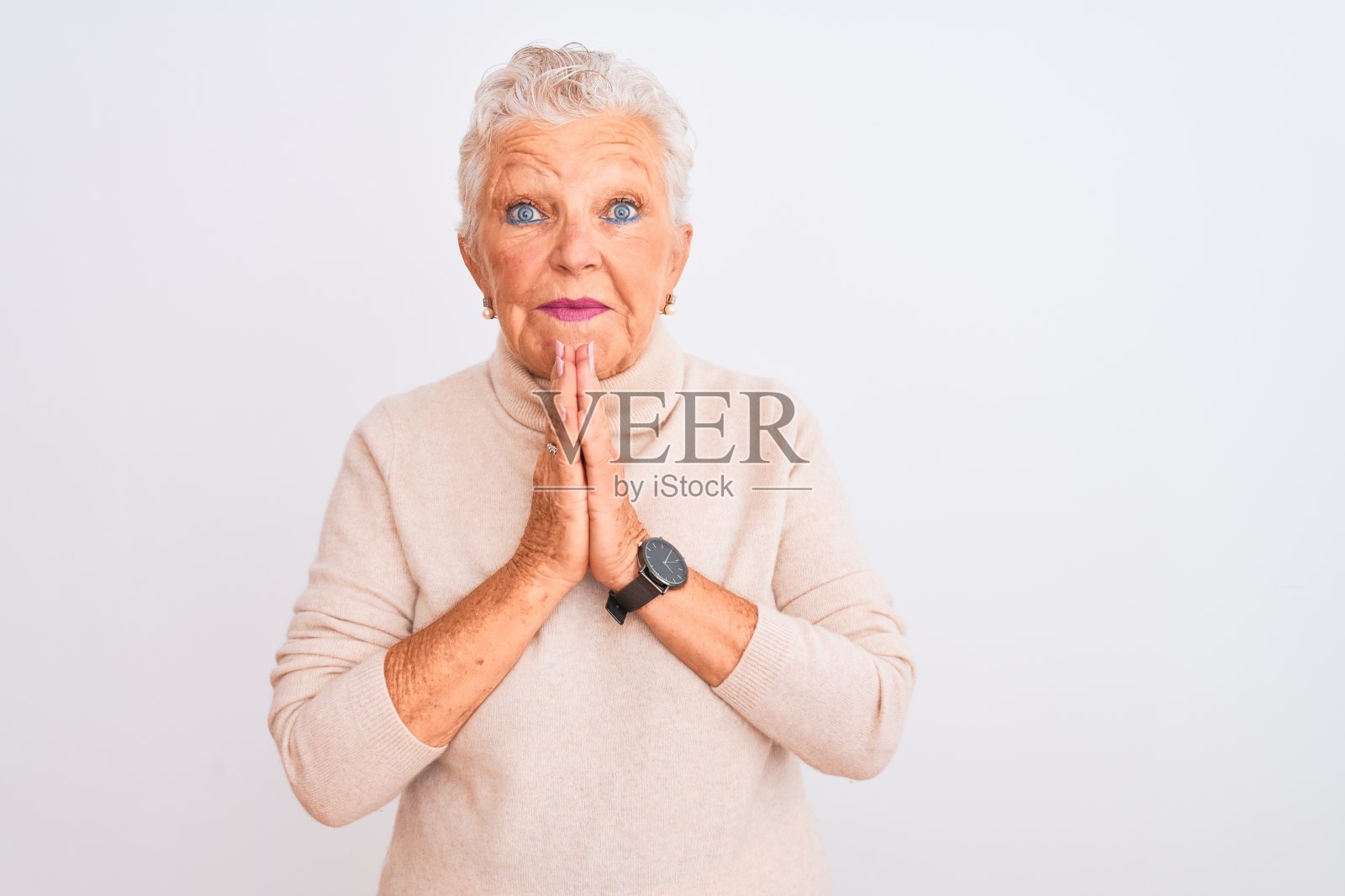 身穿高领毛衣的年长白发女性，在白色背景前双手合十祈祷，请求原谅，面带自信的微笑照片摄影图片