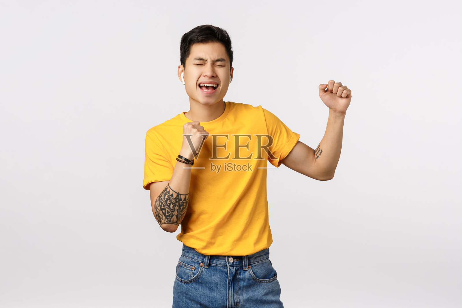 男人充满激情地唱歌，戴着无线耳机听音乐，闭着眼睛唱歌放松，在白色背景下快乐地唱卡拉OK照片摄影图片