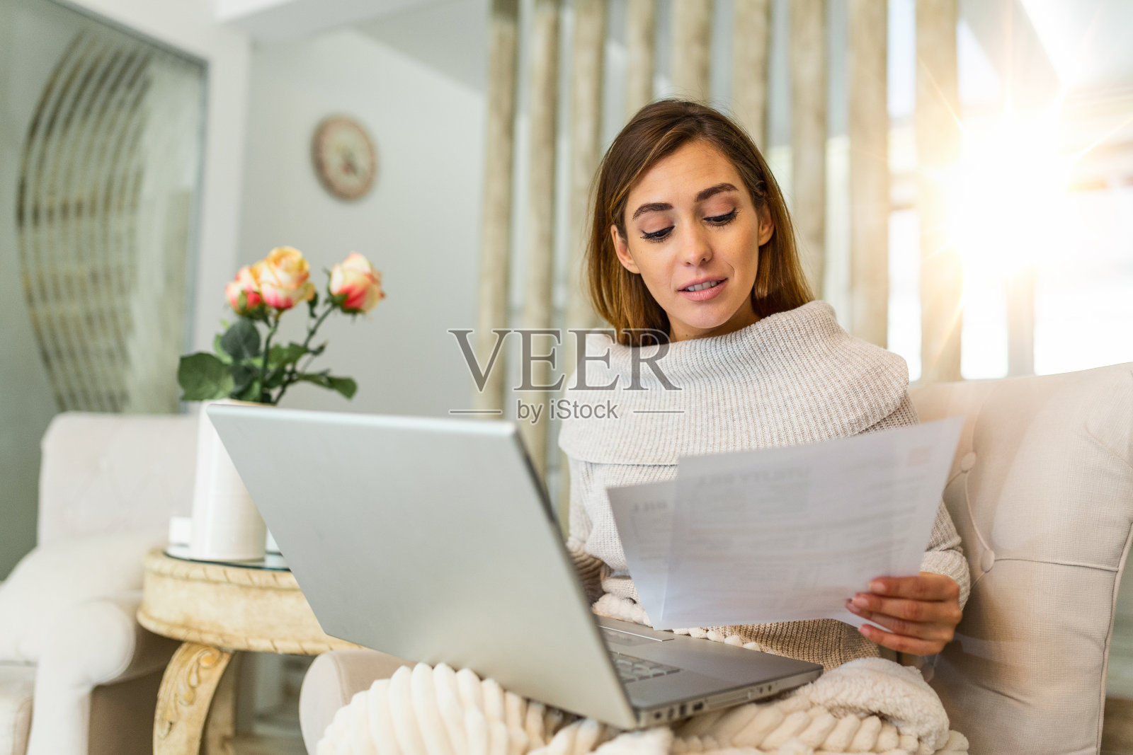 室内的照片，穿着随意的年轻女子手里拿着文件，在家里计算和支付账单。幸福美丽的女人坐在沙发上用笔记本电脑计算家庭财务照片摄影图片