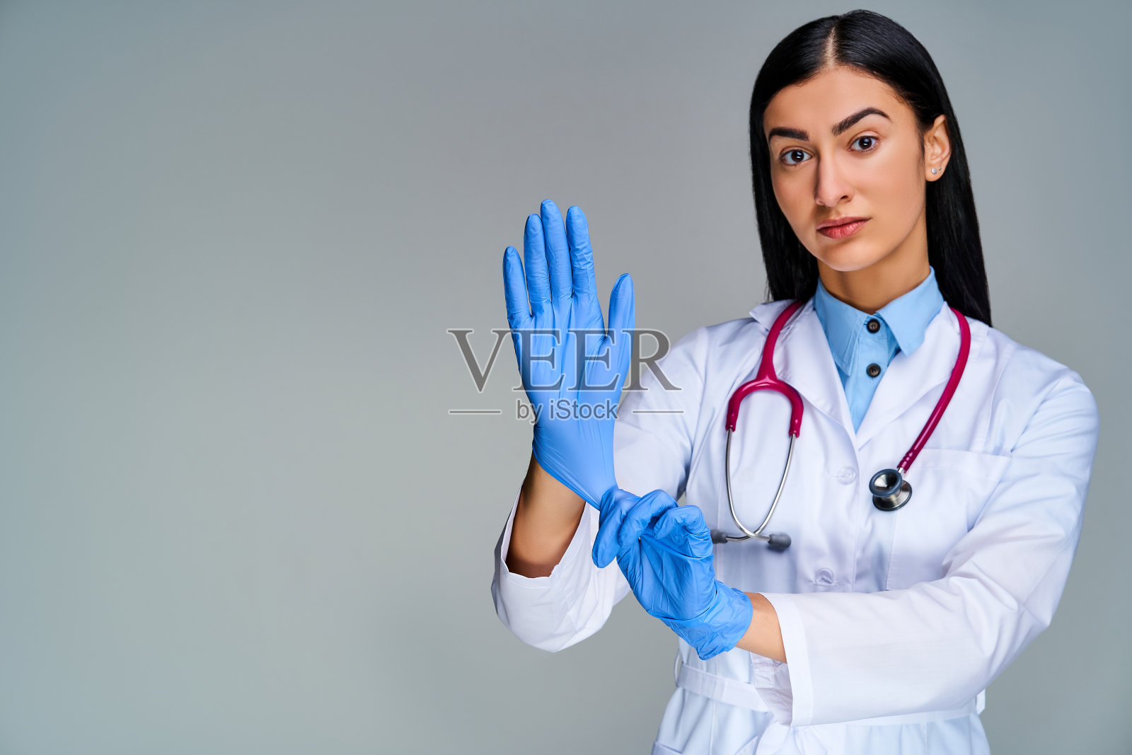 女医生穿着医用大衣，肩膀上戴着语音内窥镜，很明显地戴上了蓝色医用手套。医学的概念照片摄影图片