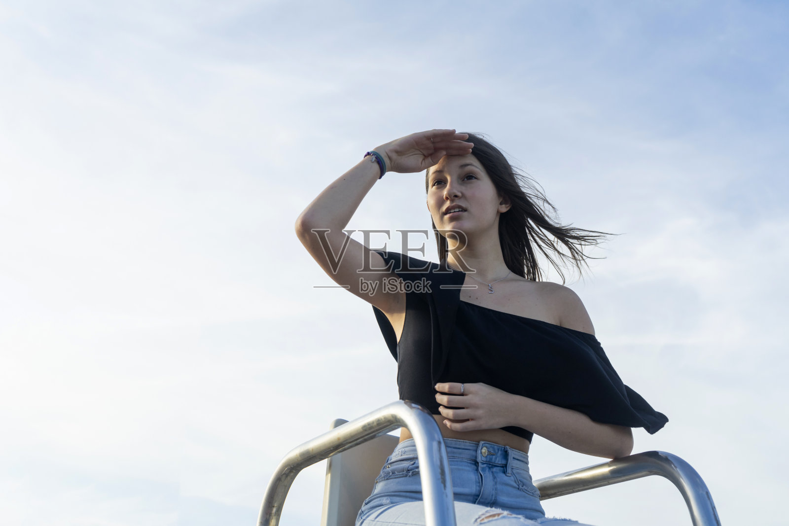 一位留着长发的年轻女子双腿交叉坐在人行道上，微笑着看向别处照片摄影图片