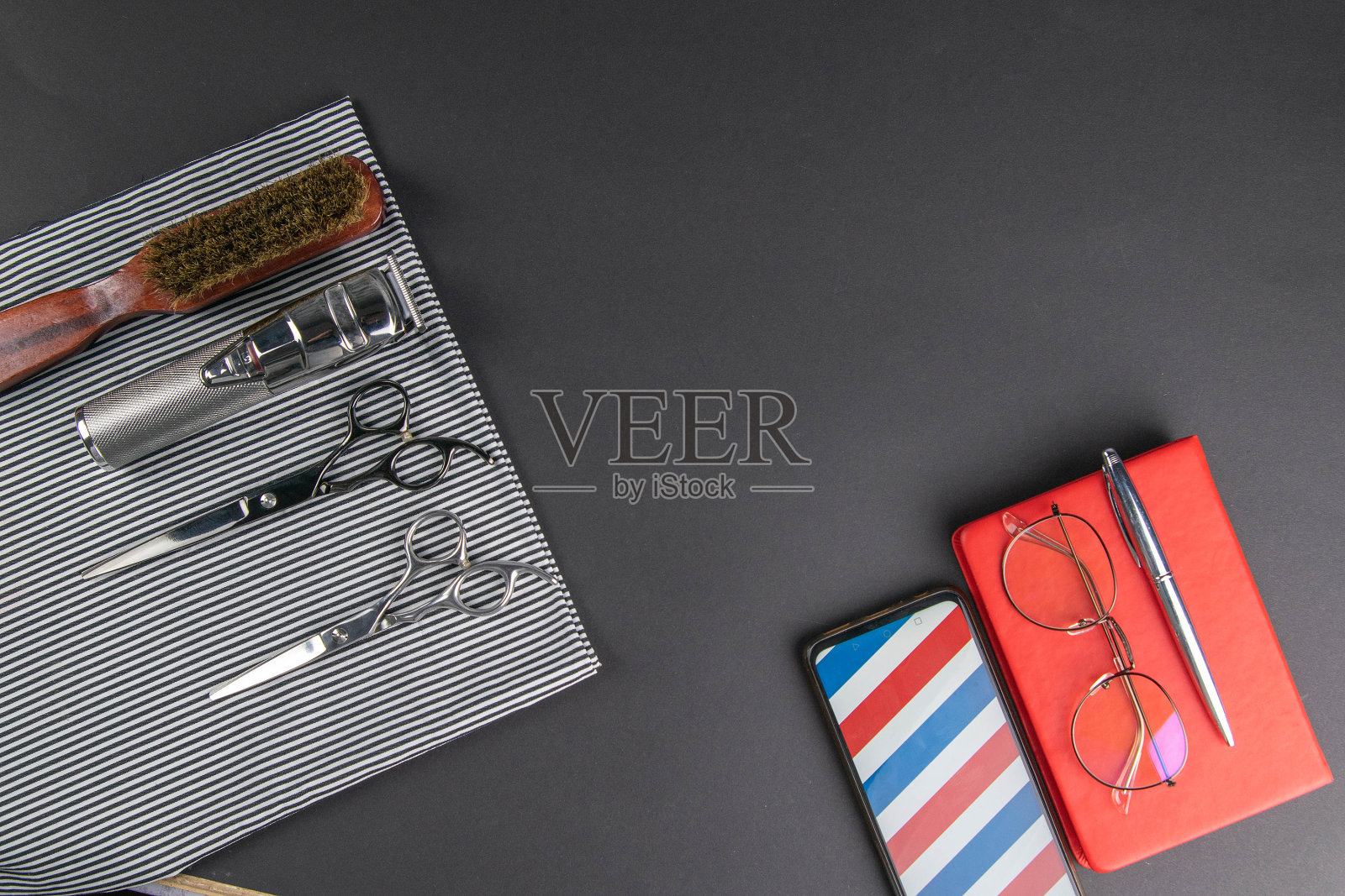 白色的毛巾上放着一台理发、剪子、梳子的机器，旁边有一部电话、一支钢笔和一个红色的笔记本，笔记本上有女人的眼镜照片摄影图片