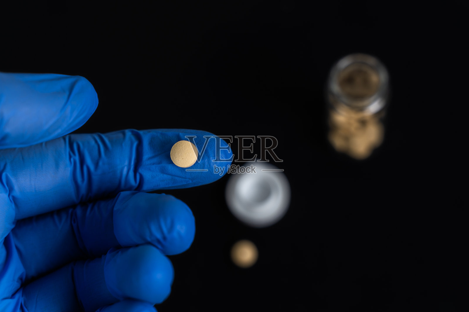蓝色橡胶手套手持小抗病毒药丸。在COVID-19和埃博拉的早期试验中，实验室研究的药物加速了冠状病毒的康复。有效对抗SARS-CoV-2病毒。照片摄影图片