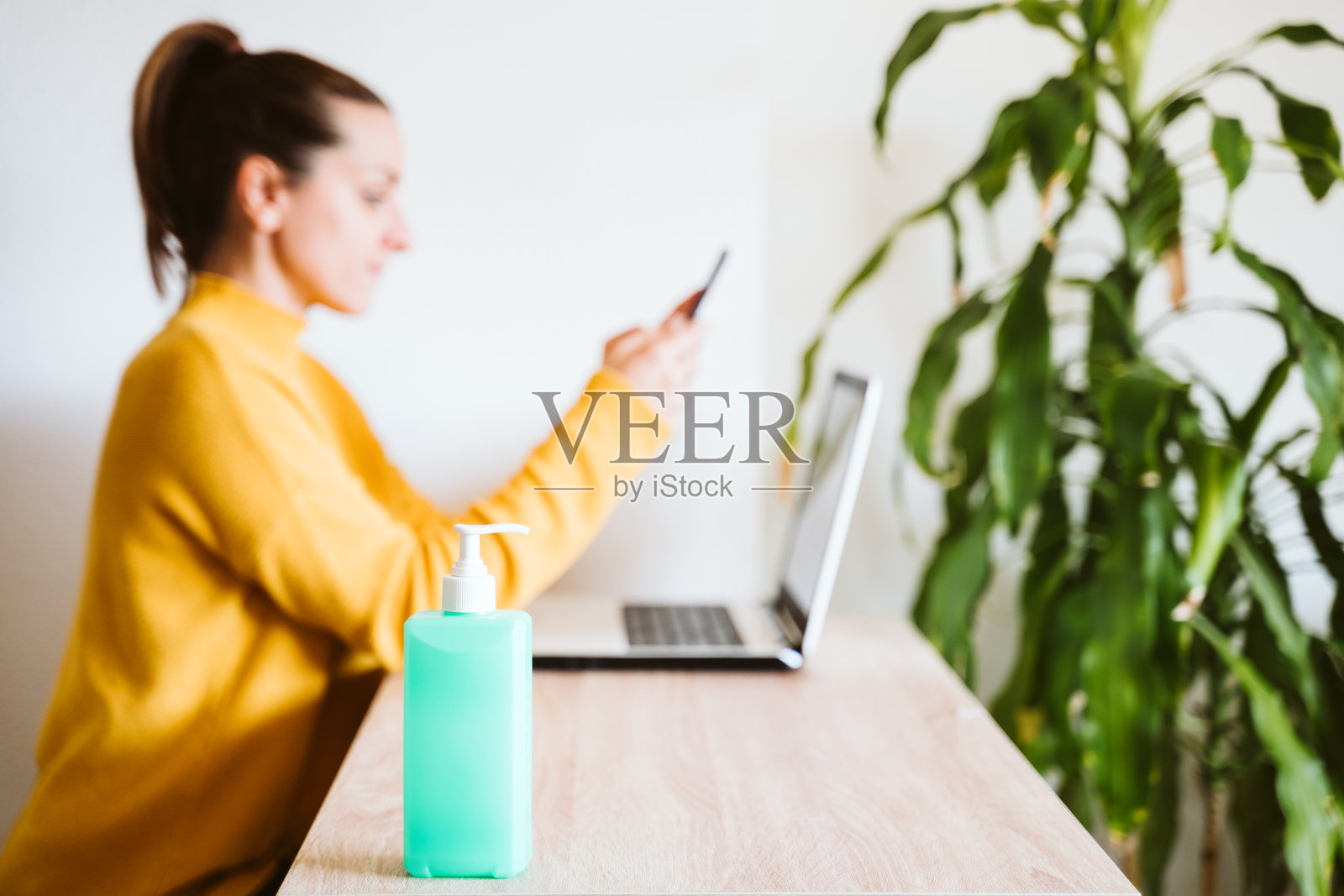 在家用笔记本电脑工作，使用洗手液的年轻女人。新冠疫情期间居家概念照片摄影图片