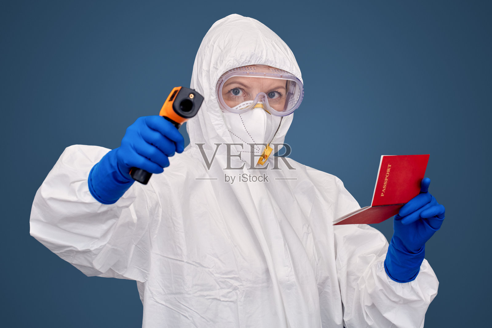 疫情概念：穿防护服的医生用红外摄像机检查发烧，蓝色隔离背景照片摄影图片