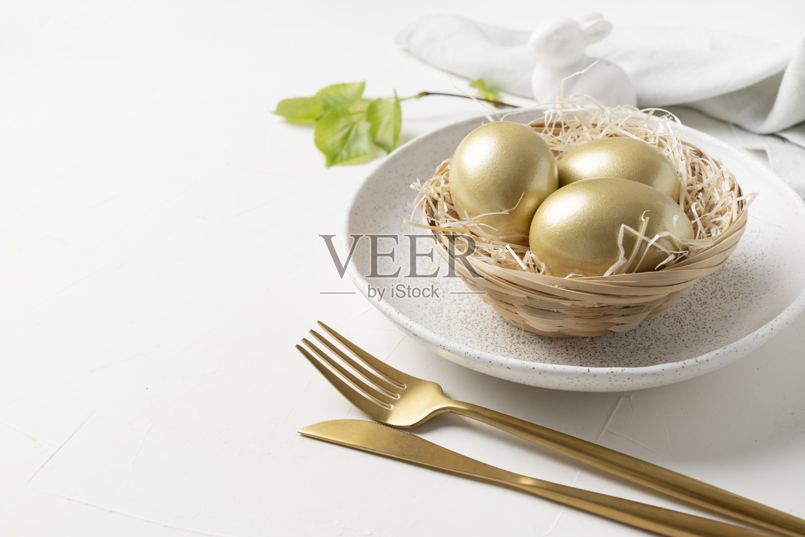 复活节餐桌上白色的桌子上摆放着兔子和金蛋。关闭了。照片摄影图片