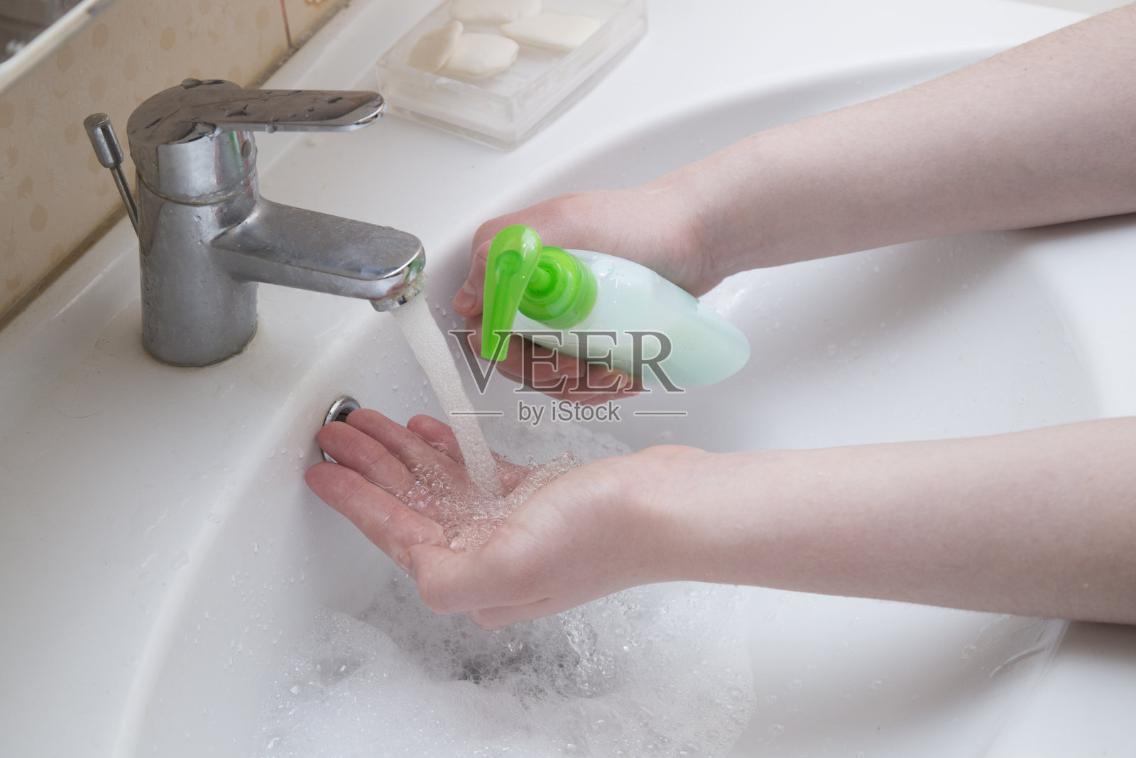 一个男人在浴室的水龙头下洗手。照片摄影图片