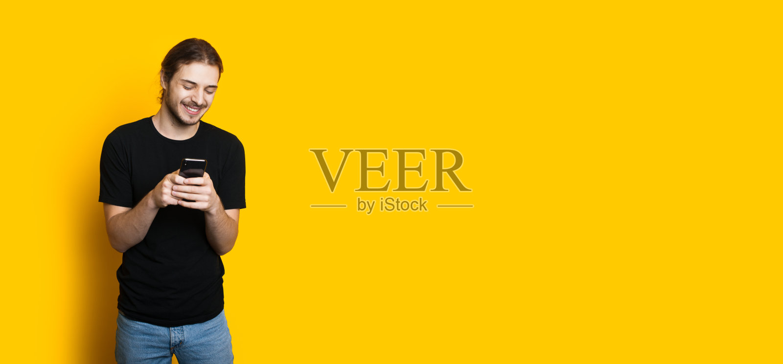 长头发留着胡子的白人男孩在黄色背景下用手机发短信照片摄影图片