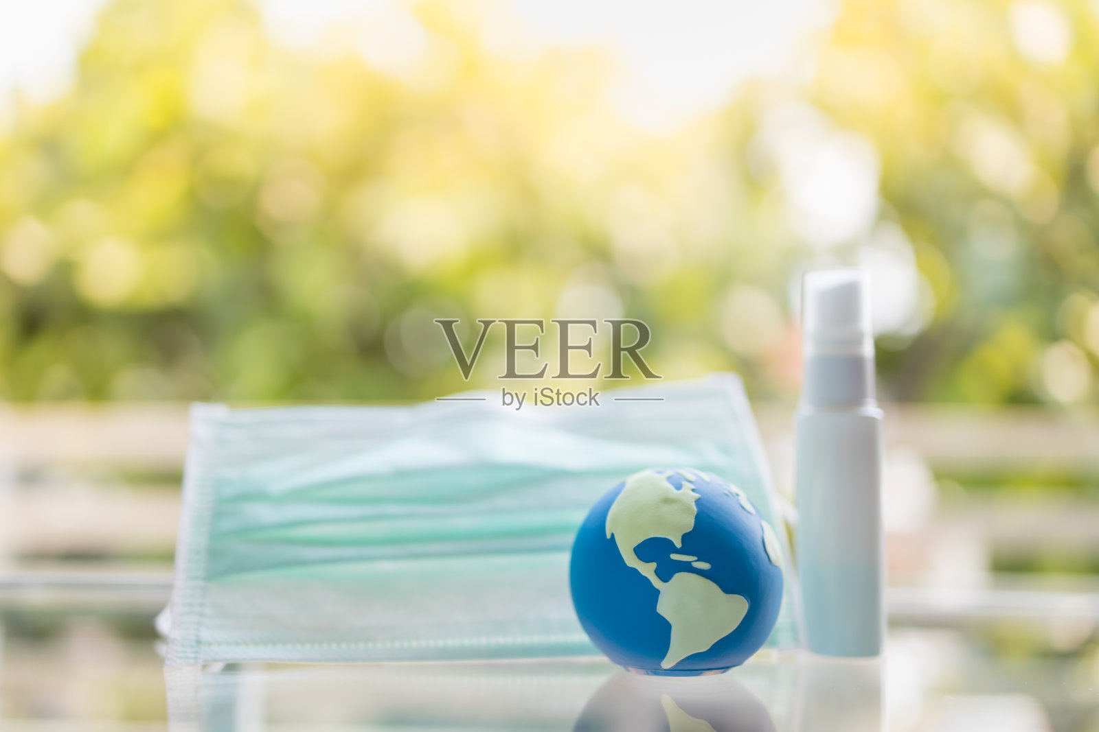 全球医疗、冠状病毒、Covid-19防护理念。特写微型世界球外科口罩和迷你瓶酒精喷雾与绿色自然背景。照片摄影图片