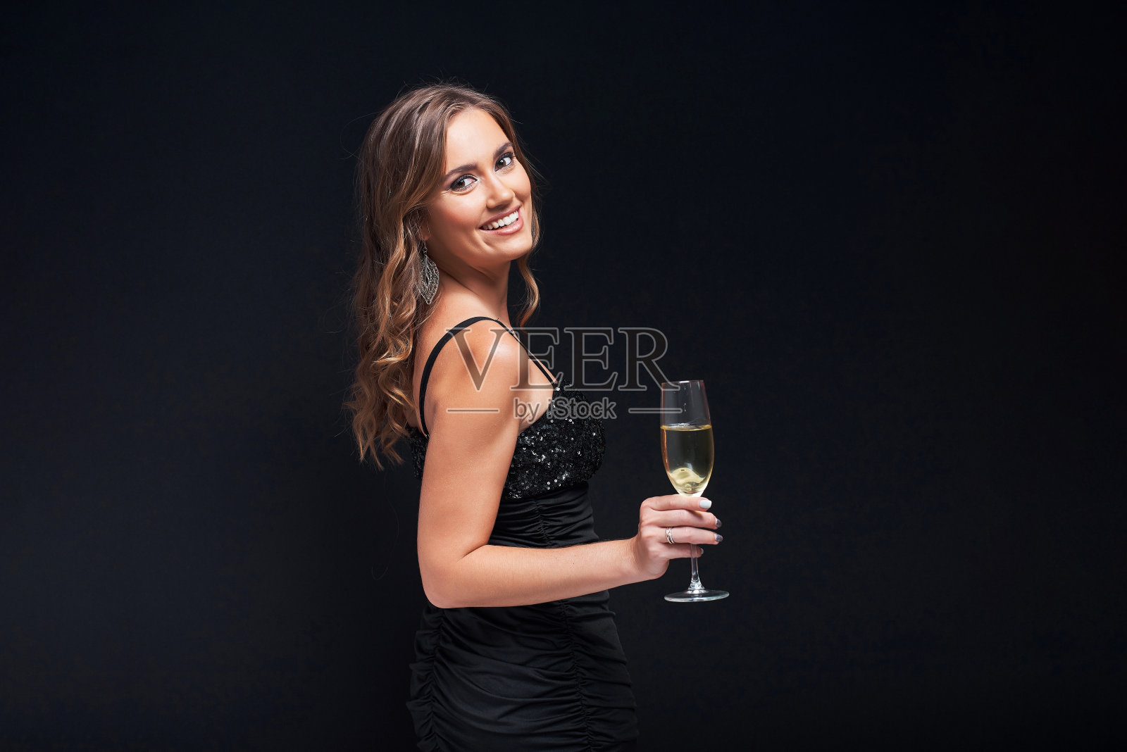 年轻女子在优雅的裙子与一杯香槟在黑色的背景。照片摄影图片