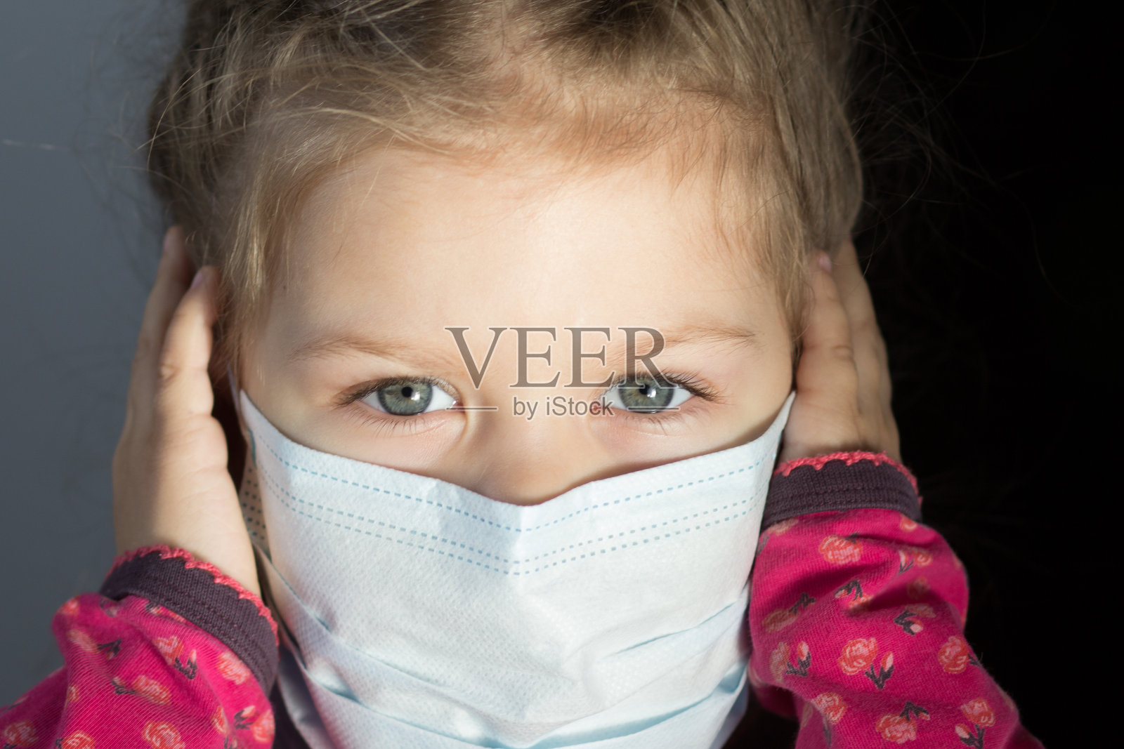 3岁的白人孩子的肖像与面具在脸上看着照相机，并在灰色的背景上握着她的手照片摄影图片
