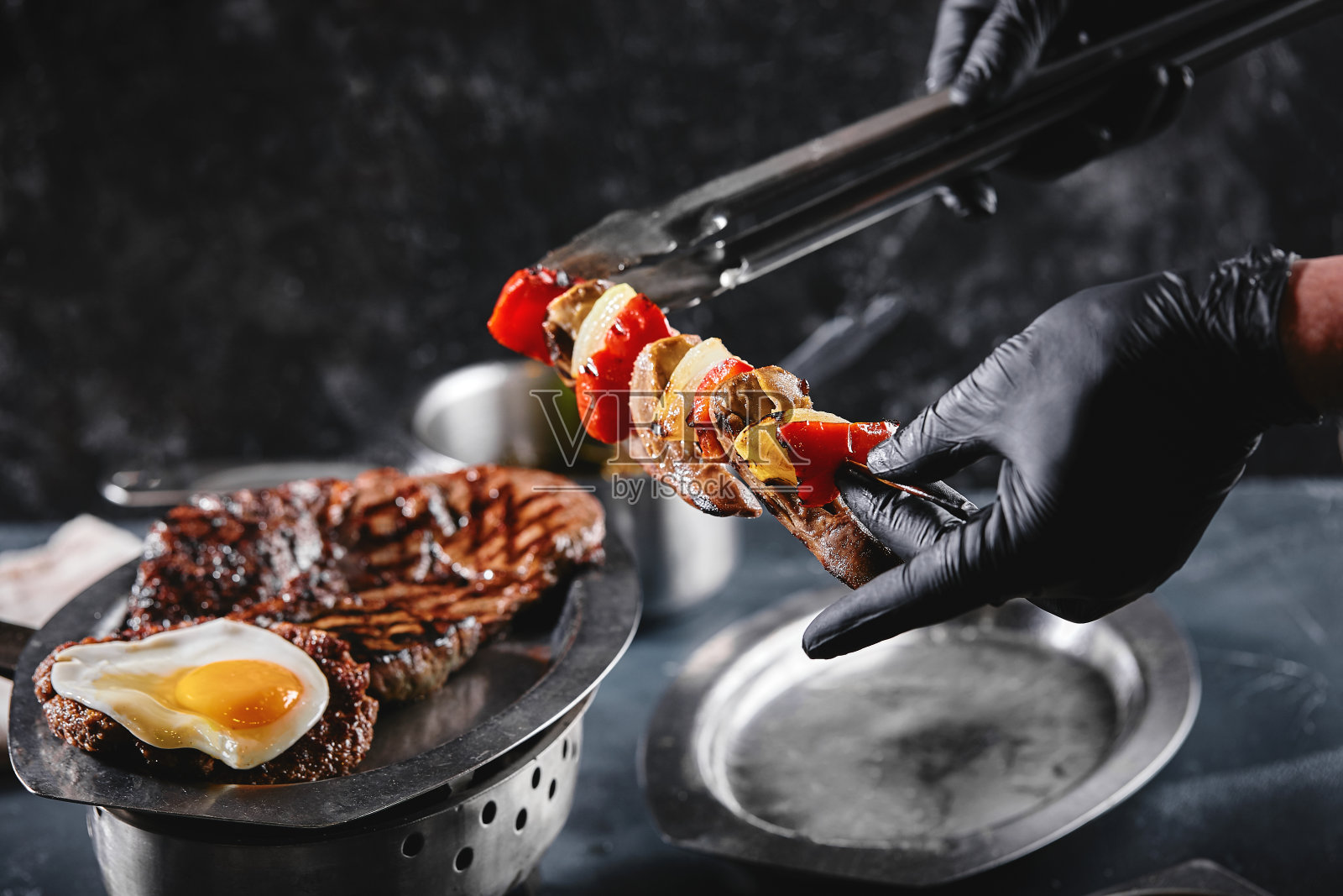 烤肉拼盘。什锦美味的烤肉配蔬菜。烤杂烩肉配辣椒酱和蔬菜。厨师用手把肉摊在盘子上照片摄影图片