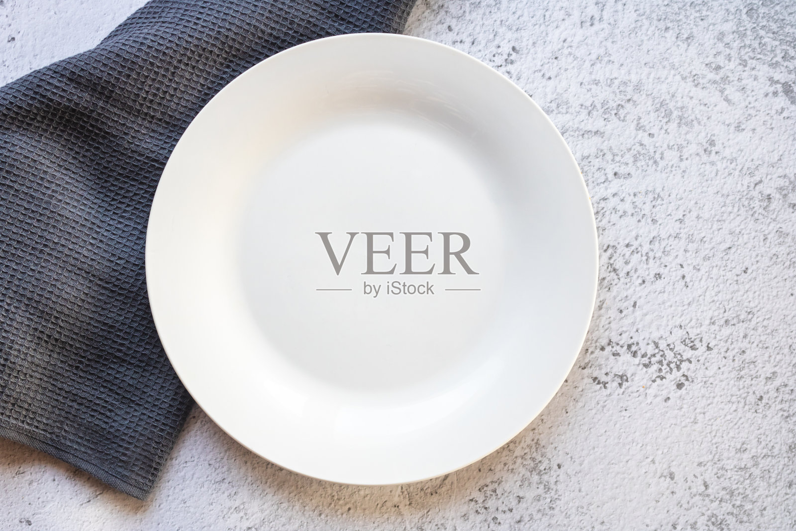 白色的混凝土上，放着一个白色的盘子，旁边是一条灰色的厨房毛巾照片摄影图片