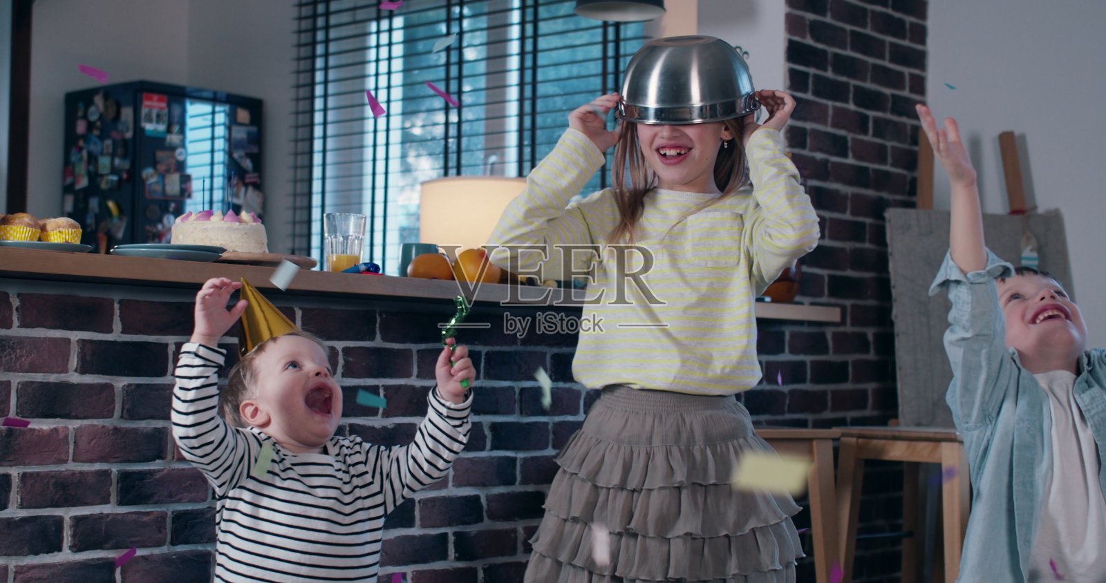 可爱快乐的少女在空中扔五彩纸屑庆祝生日派对与两个小弟弟的慢镜头。照片摄影图片