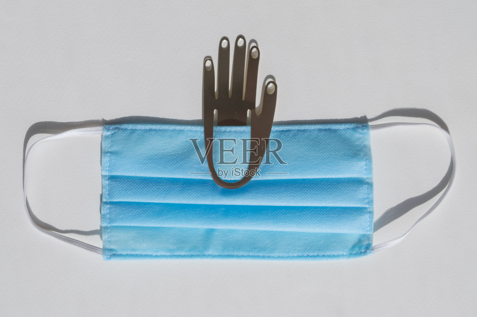 金属手戴浅蓝色医用一次性口罩，白色背景，对抗2019冠状病毒。医疗理念，遏制冠状病毒照片摄影图片