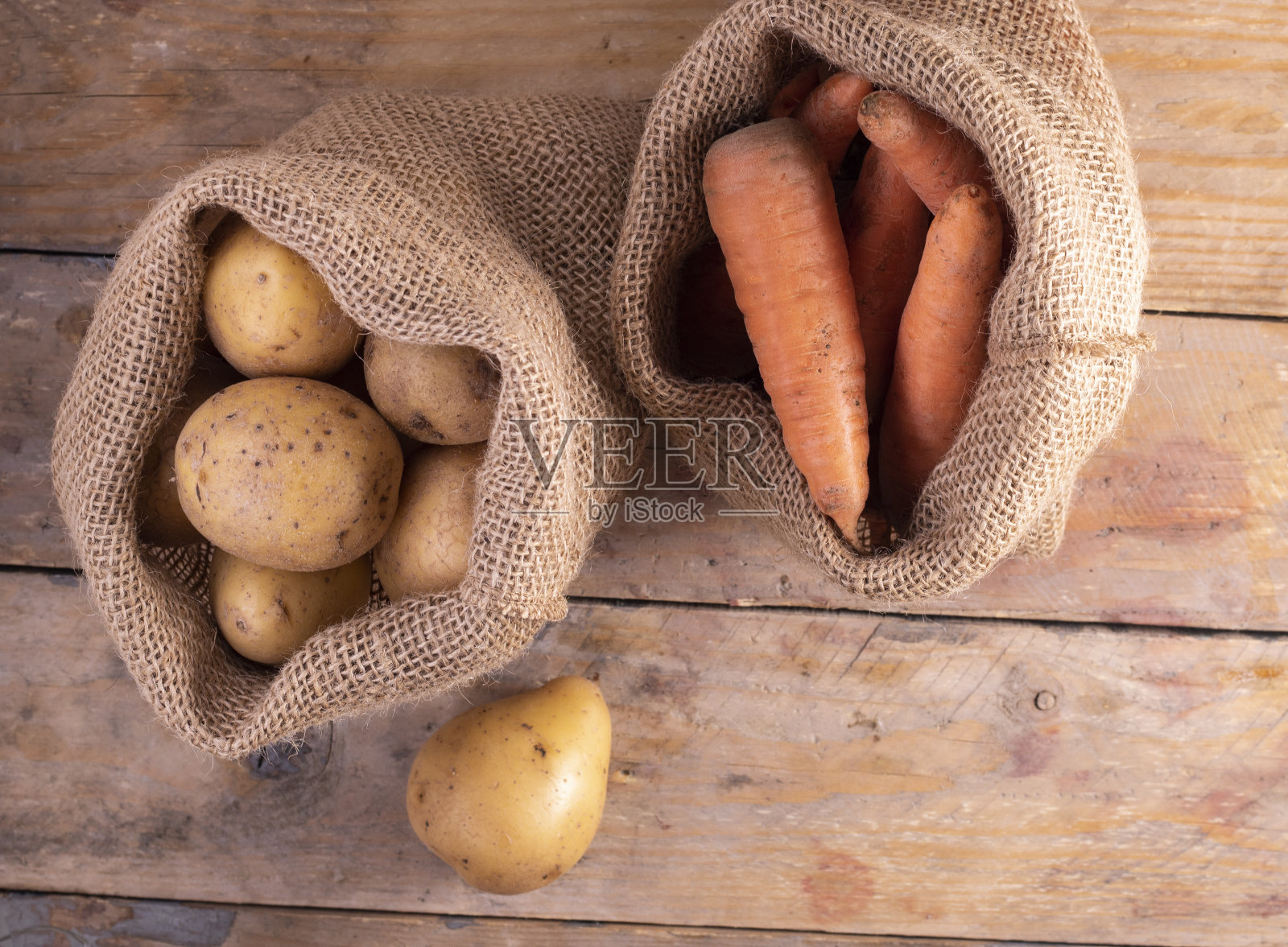 木桌上裹着麻布袋的土豆和胡萝卜。生态的概念照片摄影图片