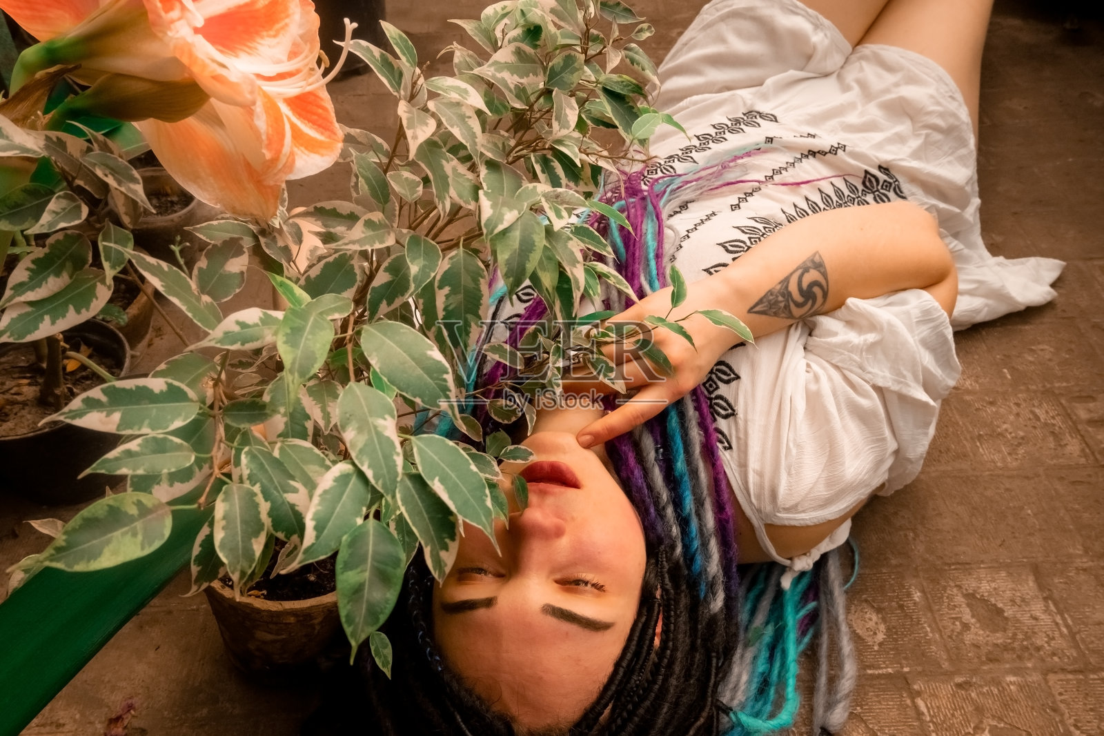 身穿白色连衣裙的彩色脏辫美女，躺在橙色楼梯下的植物中，乌克兰第聂伯植物园的热带植物温室，面部大特写照片摄影图片