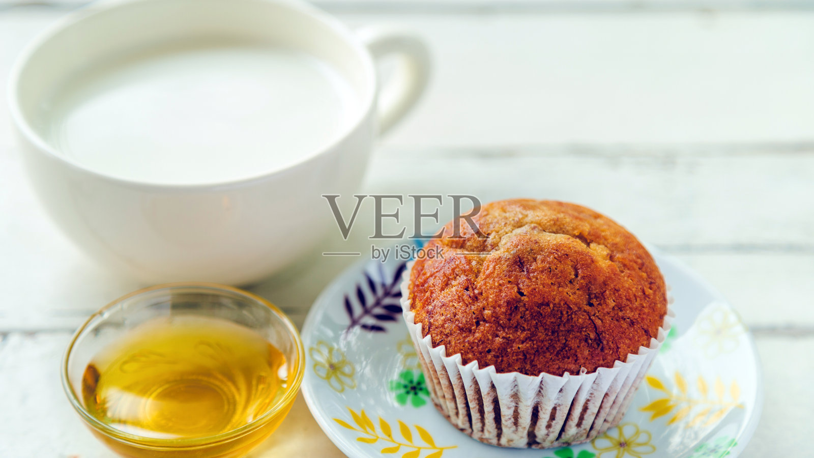 靠近香蕉蛋糕在白色盘子与蜂蜜和一杯牛奶在木桌上。照片摄影图片