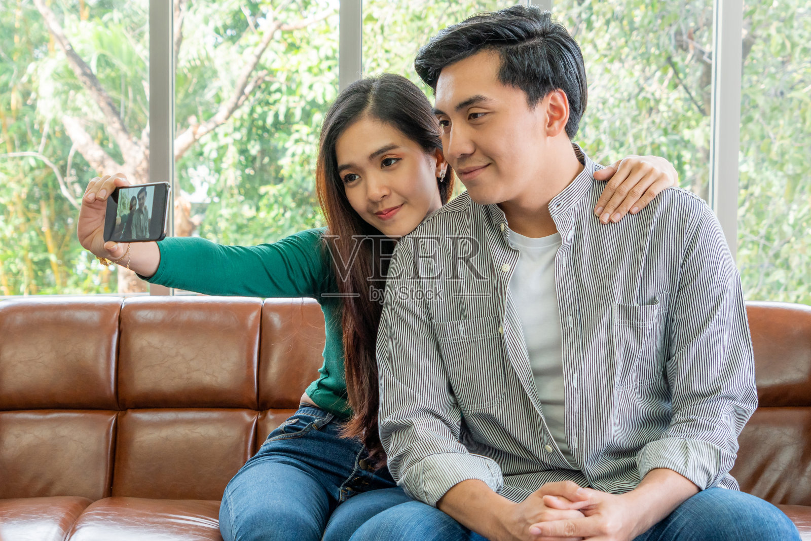 幸福的亚洲情侣喜欢在家里的客厅用手机自拍。照片摄影图片