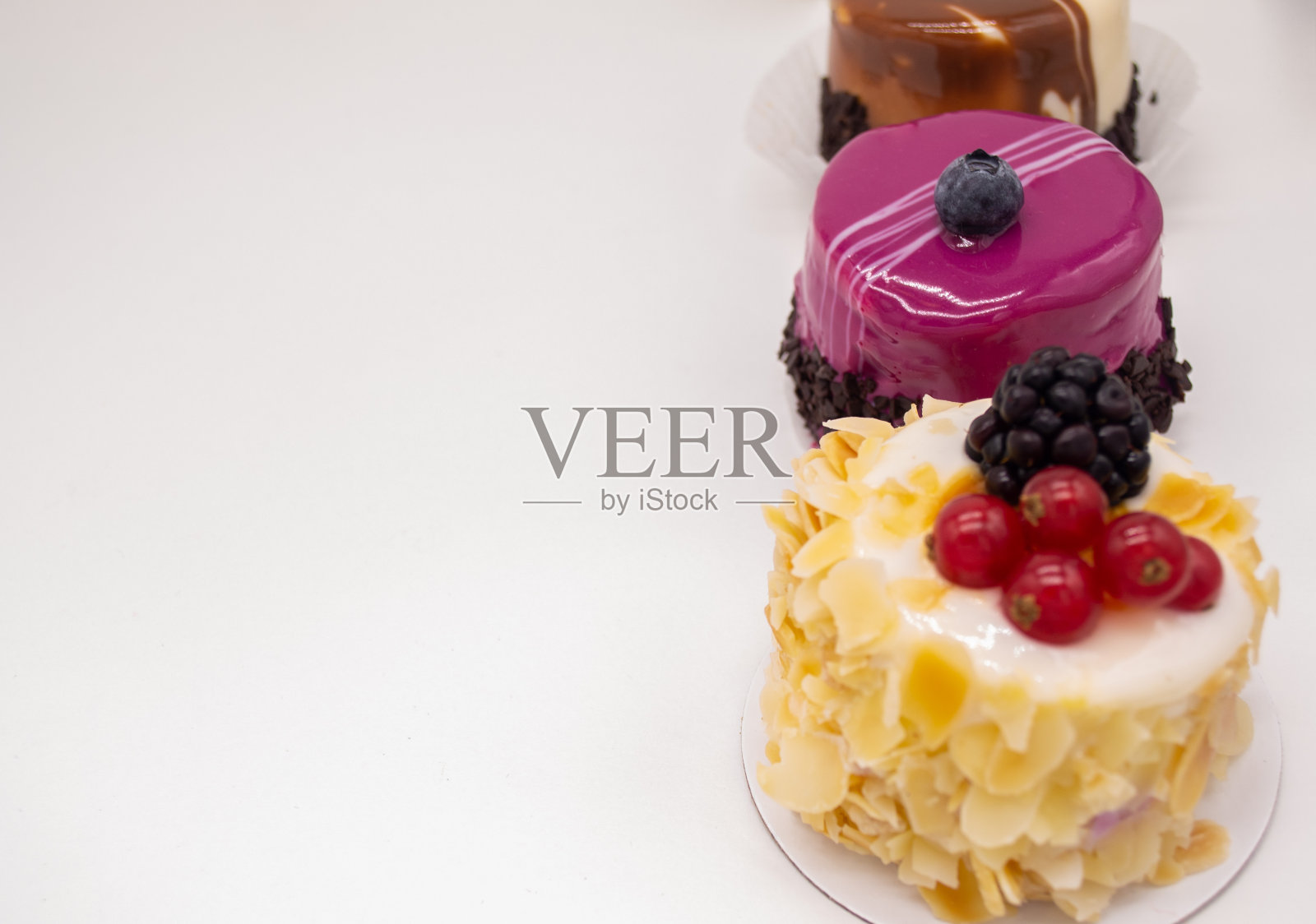 白色背景上的三个蛋糕:咖啡蛋糕和一粒咖啡，巧克力，杏仁花瓣奶油蛋糕，红醋栗和黑莓，粉色慕斯和蓝莓和巧克力片。本空间照片摄影图片