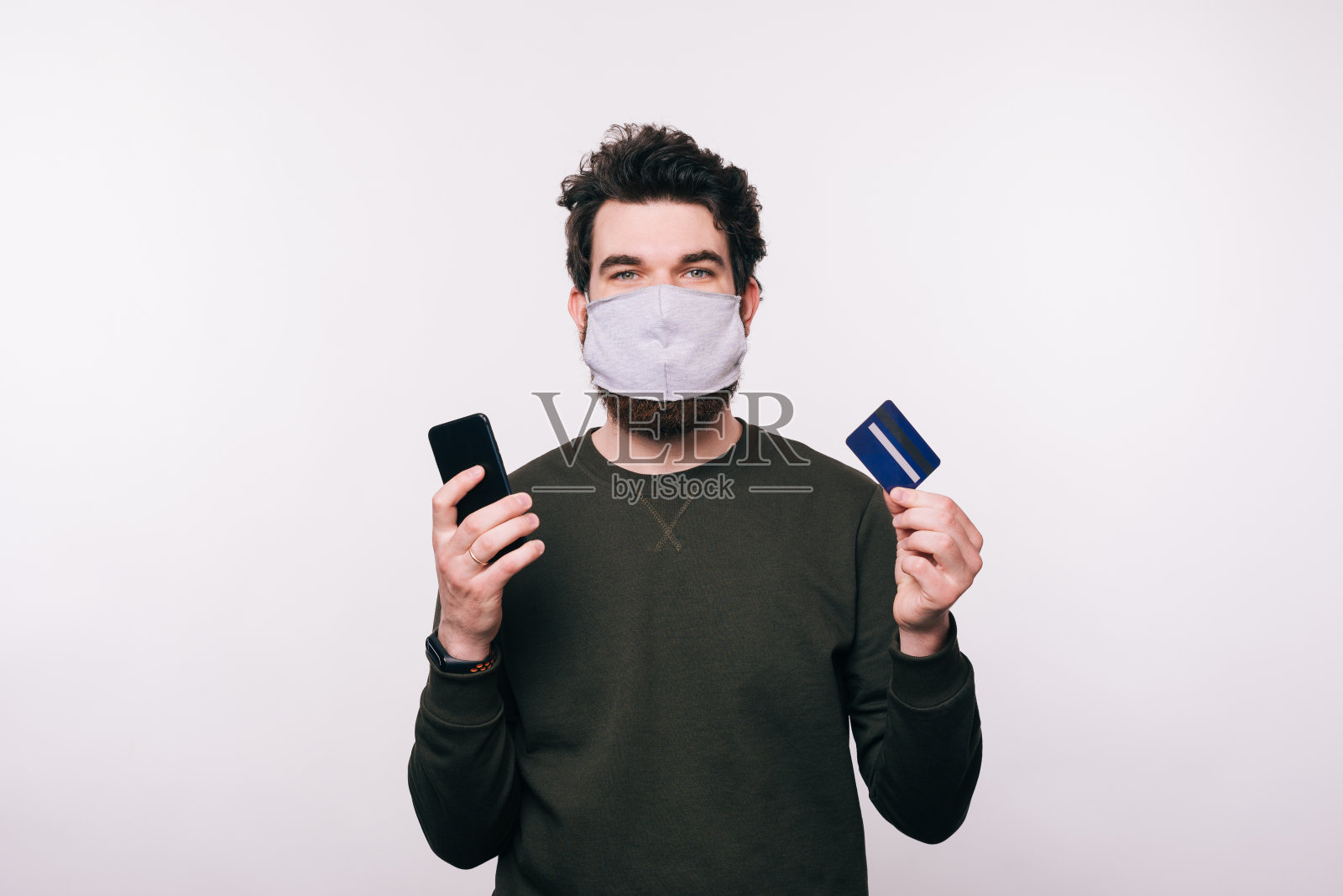 一名戴口罩的男子在白色背景下使用智能手机和信用卡照片摄影图片