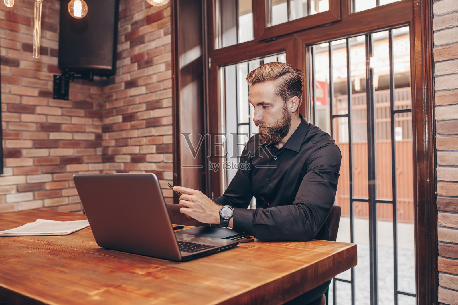 年轻的商人坐在咖啡馆里一边用智能手机发短信一边用笔记本电脑工作照片摄影图片