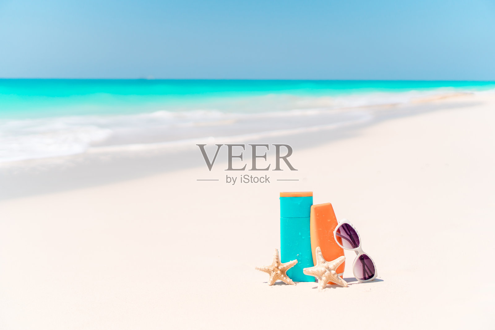 防晒霜瓶子，护目镜，海星和太阳镜在白色的沙滩背景海洋照片摄影图片