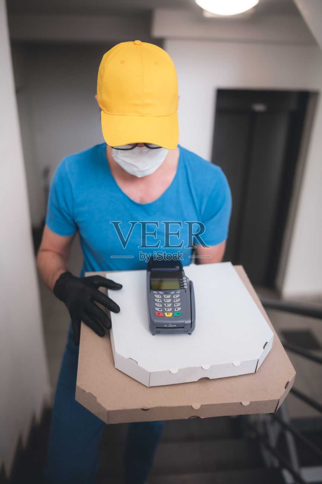 送餐员带防护医用口罩，手持披萨盒和POS无线终端支付卡-病毒和大流行天，食品送至您的家和安全卫生措施。照片摄影图片