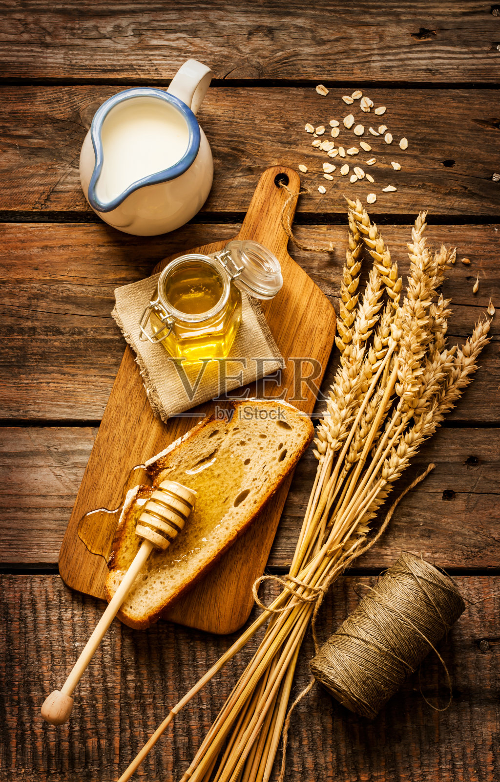 罐子里装蜂蜜，面包片，小麦和牛奶放在老木头上照片摄影图片