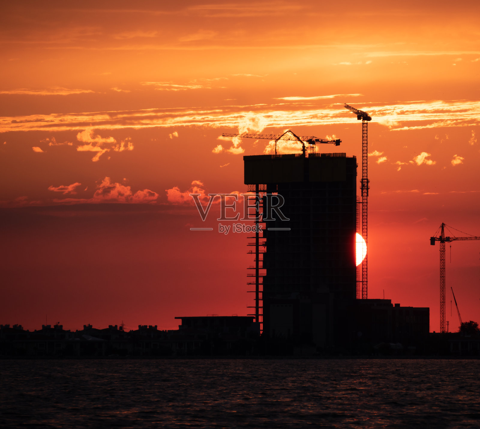 建筑与摩天大楼和起重机映衬着阳光下五彩缤纷的天空。照片摄影图片