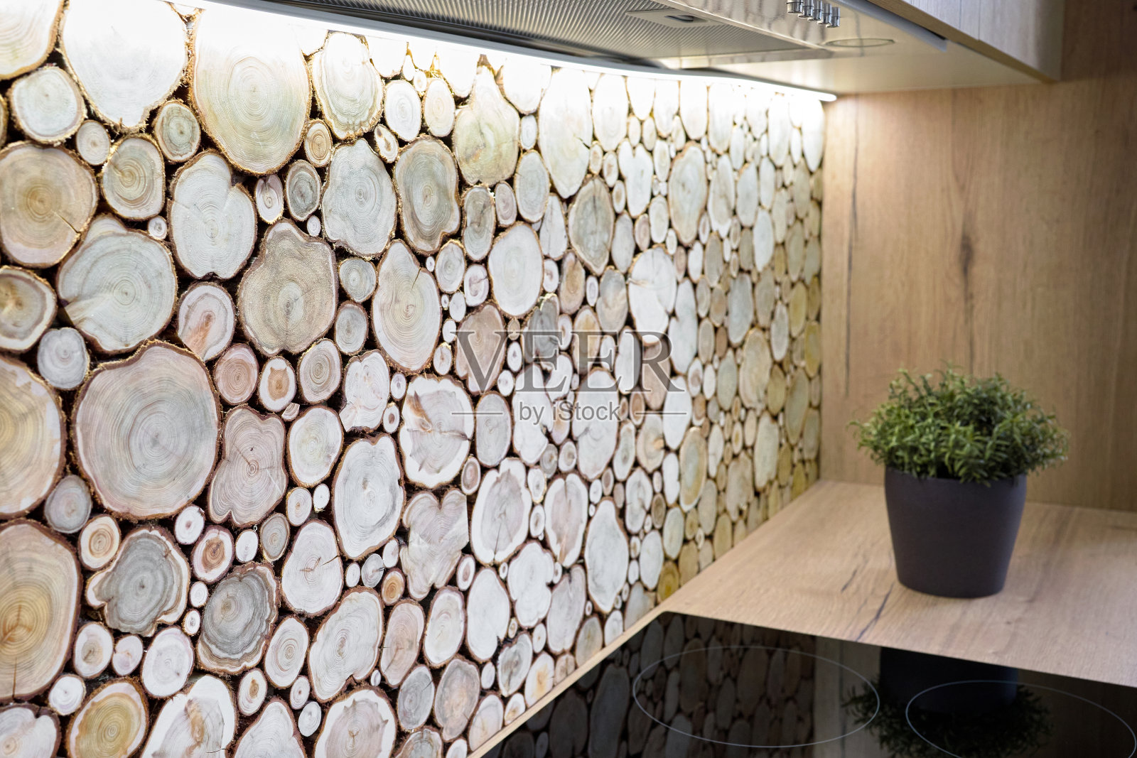 现代厨房内部用滚刀和台面后面装饰着墙壁上的树干，树干被切割成圆木，放在一起作为室内装饰。照片摄影图片