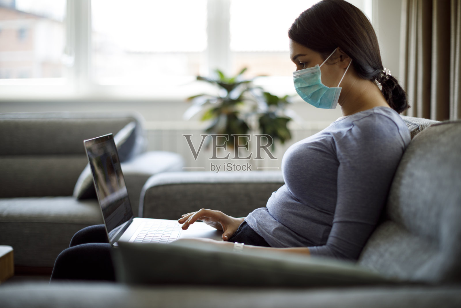 年轻女子戴着防护口罩在家使用笔记本电脑照片摄影图片