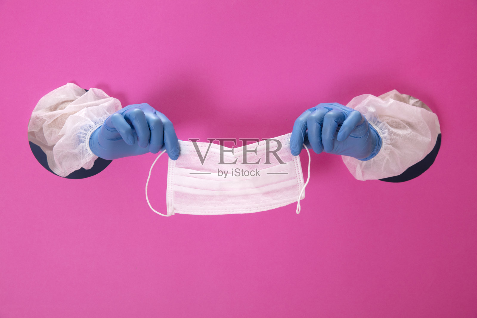 双手握着，粉红色背景上显示外科口罩。照片摄影图片