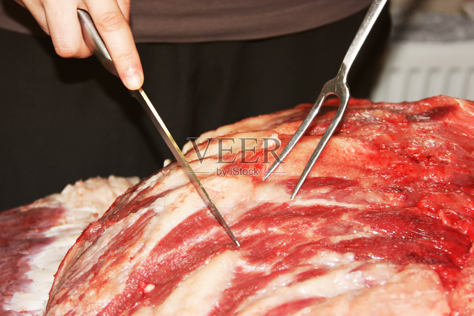 一个男人切新鲜的肉。猪肉。刀和叉照片摄影图片