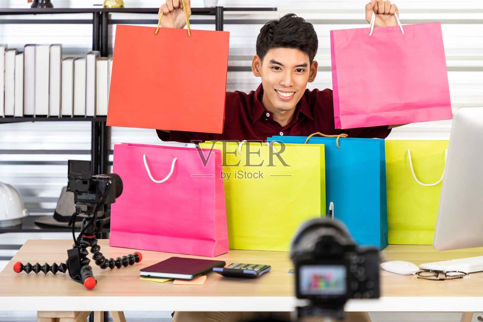 年轻的亚洲男性网上商人博主用相机直播视频，展示购物袋。社交媒体和在线影响者的概念。照片摄影图片