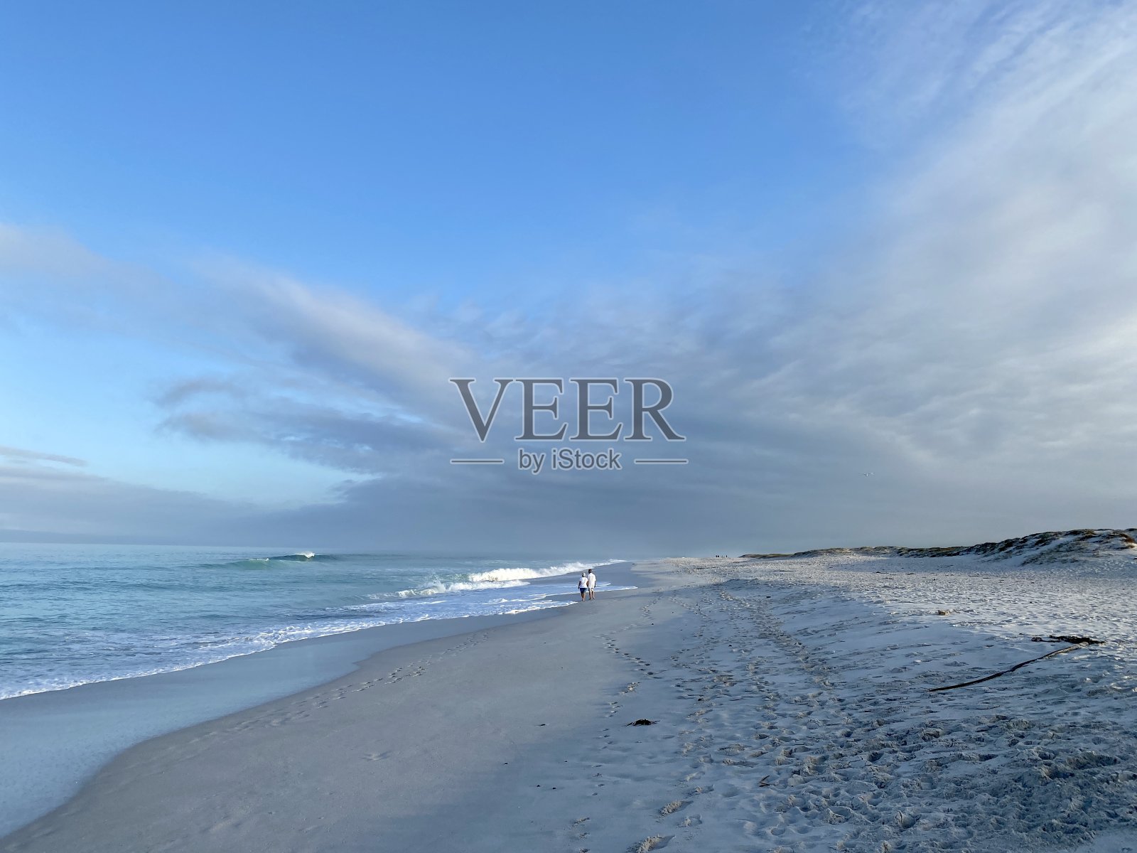 一对老年夫妇在远处的海滩上散步照片摄影图片