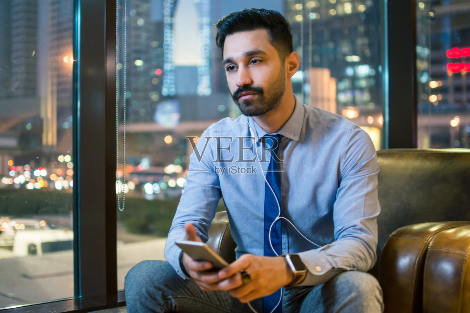 在办公室舒适沙发上用智能手机听音乐的英俊年轻商人照片摄影图片