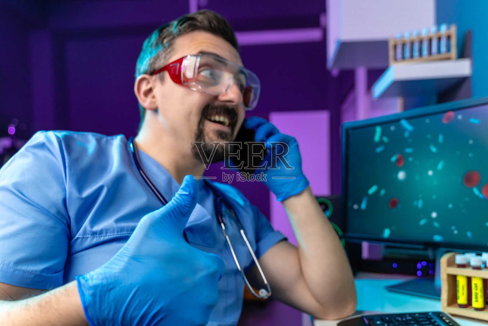 快乐的医生戴着防护眼镜在他的手机上交谈，并竖起大拇指照片摄影图片