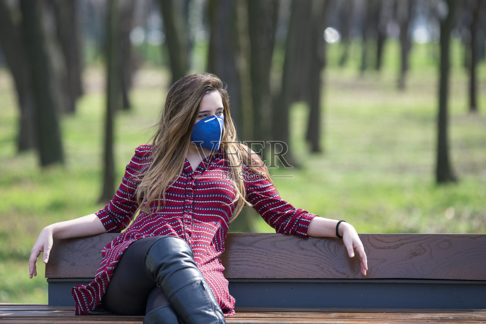 坐在公园长椅上，戴着防护面具的女人。冠状病毒的概念。照片摄影图片