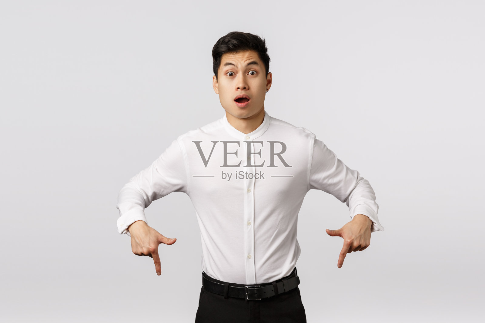 吓坏了，惊慌和惊讶震惊的亚洲帅哥穿着衬衫，裤子，指着下，惊讶地喘着气，说不出话来，说哇，听到奇怪的意想不到的消息，白色的背景照片摄影图片