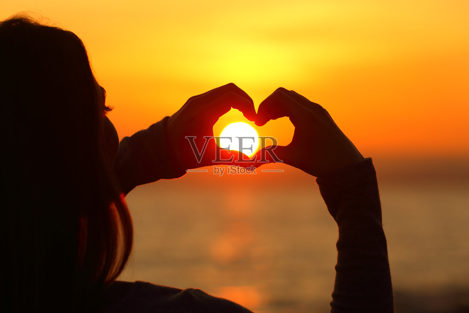 女孩手的剪影在太阳周围做出心形照片摄影图片