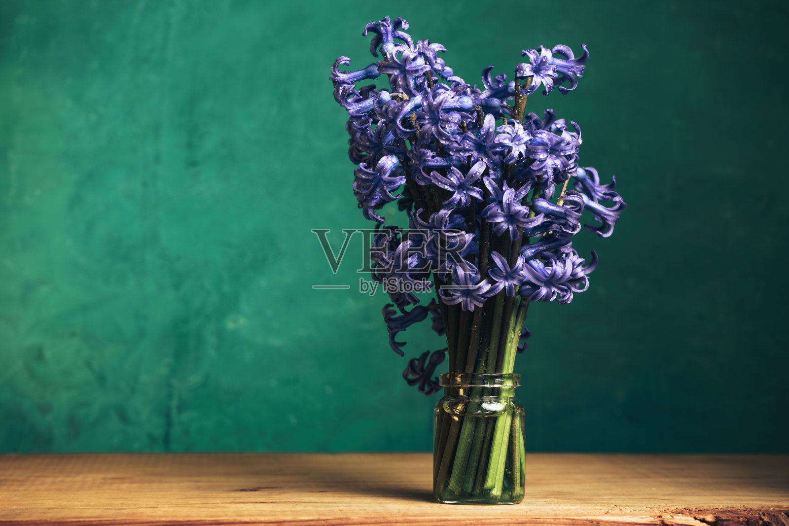 红色的木桌和绿色的墙壁背景上，花瓶里插着漂亮的紫色风信子花。照片摄影图片